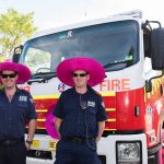 Two firefighters in pink hats in front of a fires truck
